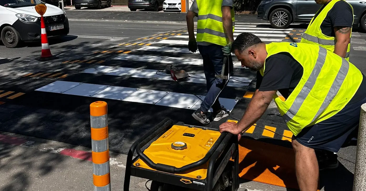 Montaj de limitatoare de viteza din cauciuc la o trecere de pietoni, de catre muncitori in veste reflectorizante